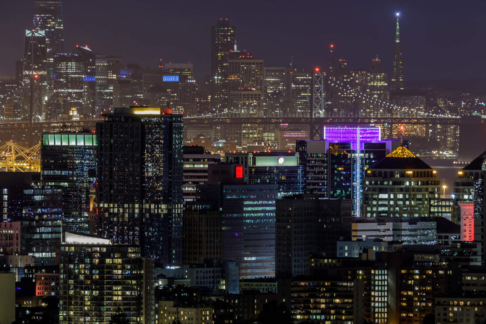 Oakland California office buildings at night with San Francisco skyline and Bay Bridge in background